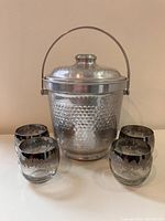 Metal ice bucket with hammered chrome finish, handle, and lid, showing minor dents and shine