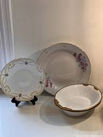 Front view of the vintage Limoges dining set showing bowls, shallow platter with floral design, and decorative plate with gold gilding.