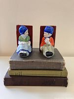 Front view of vintage Dutch girl and boy ceramic bookends seated on stacked books with colorful paint details.