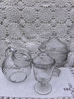 Shot of the 2 pedestal bowls and ball-shaped pitcher together on white cloth with lace background.