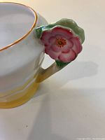 Close-up of the creamer's ornate pink flower handle with green leaves, showing detailed hand-painting and gold trim