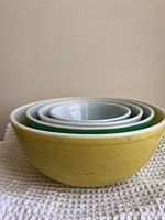 Side view of stacked vintage Pyrex bowls showing yellow exterior of largest bowl, with visible wear and marks on surfaces.