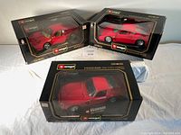 Three boxed Bburago Ferrari die-cast model cars: 250 GTO (1962), Ferrari GTO (1984), Ferrari F40 (1987) shown together on white cloth