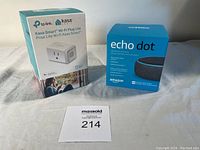 Echo Dot 3rd generation box and Kasa Smart Wi-Fi Plug Lite box side by side on white fabric surface.