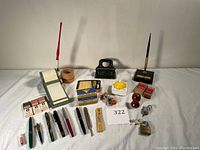 Overview of various vintage fountain pens, vintage rubber stamps, ink cartridges, hole punch, padlock, pencil sharpener, paper roll dispenser, and thumb tacks box.