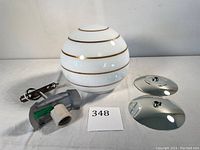 White glass globe with gold stripes placed next to mounting hardware and chrome plates.