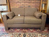Front view of brown fabric loveseat on patterned rug, showing two seat cushions and two bolster pillows.