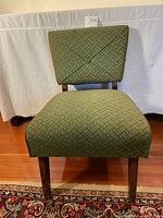 Front view of Mid Century Modern slipper chair showing green geometric patterned upholstery with a button detail on the backrest and wooden legs.