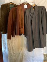 Four men's outerwear items hanging: long grey coat, two brown wool jackets, and one corduroy jacket.