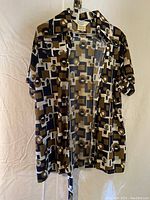 Men's short-sleeve geometric patterned button-up shirt with chest pockets, hanging on hanger in front of white backdrop.