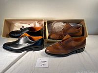 Pair of black Oxford shoes and brown brogue shoes displayed with original boxes and lot card.