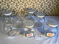 Full set of 6 vintage Miracle Whip glass jars with white lids on white cloth background and patterned wallpaper.