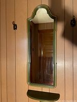 Vertical green framed mirror mounted on wall with green shelf below it.