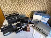 Wide view of all items included: multiple radios, scanner in box, answering machine, and calculator.