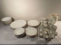 Full set of white ironstone dishes, plates, mugs, egg cups, and two pitchers with silver trim displayed on table.