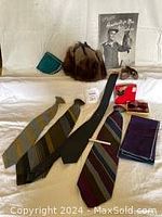 Photo of assorted mens accessories including ties, notebook, muskrat hat, and pattern book on white sheet background.