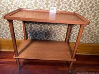 Front view of the wooden tea trolley showing two shelves and four legs with small caster wheels.