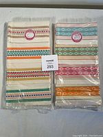 Three heritage brand tea towels still in original packaging with colorful stripe designs on cream background.