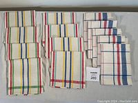 Three groups of folded vintage tea towels. Left group has yellow, green, red, blue stripes on cream background. Center group has red, yellow, blue stripes on cream. Right group has red and blue stripes forming plaid pattern on cream.