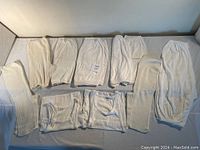 Multiple vintage white undergarments including long bloomers, shorter bloomers, undershirts, and ribbed socks arranged on flat surface