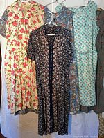 Four vintage dresses hanging on hangers showing varying floral and patterned prints in different colors and styles.