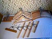 Photo showing full set of vintage wooden hangers including coat hangers, slacks hangers, and skirt hangers with clips arranged on white surface.