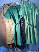 Six vintage women's dresses hanging on hangers, varied colors and patterns, displayed front view.