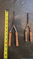 Two antique curling tongs laid side by side with a measuring tape showing approximately 7.5 inches length.