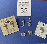 All six items displayed on a blue background. Includes palm tree earrings on card, four silver-colored beach charms, sterling silver manatee charm on card.