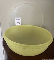 Yellow large mixing bowl with clear lid beside it on dark wood surface, showing size and color.