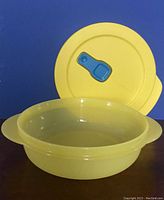 Yellow round vented microwave bowl with its lid. The vent on the lid is blue and can be opened or closed. Bowl is empty, showing interior and vent functionality.