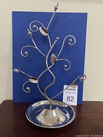 Full front view of silver-tone metal jewelry holder with curly branches and leaf decorations on a shiny metal tray base.