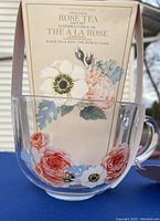 Photo of clear glass mug with rose and other floral designs and cream colored Rose Tea box inside mug.