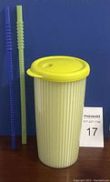 Yellow Tupperware insulated tumbler with lid standing upright alongside two straws, one blue and one green.
