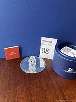 Swarovski crystal dog figurine seated on round display mirror beside original blue box with lid and a small folded pamphlet.