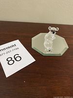 Full view of Swarovski crystal koala figurine on octagonal mirror base placed on wooden surface next to a MaxSold lot number card.