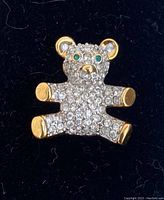 Front view of the Swarovski teddy bear lapel pin showing full crystal coverage and gold-tone details on paws and nose.
