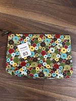 Front view of a rectangular pouch with a multi-colored floral pattern showing the entire pouch on a wooden floor.