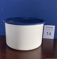 White cylindrical plastic Tupperware canister with navy blue lid, photographed against a blue backdrop with lot number.