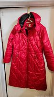 Front view of red quilted winter coat with hood visible, hanging on hanger against white background