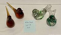 Set of four colorful glass birds arranged in a group showing front and side views, including two amber birds and two clear glass with green swirl birds.