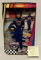 Front view of the NASCAR Barbie doll in original packaging showing the doll dressed in blue racing jumpsuit, holding helmet, with clear display packaging and checkered trim.