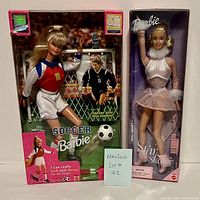 Front view of both boxed Barbie dolls: Soccer Barbie with soccer ball and Star Skater Barbie in skating outfit.