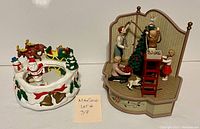 Two vintage Christmas music boxes on white surface; left is skating pond scene, right is family tree trimming scene
