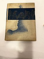 Front cover of the instructional drawing book showing tan fabric with navy blue band featuring anatomical and figure line drawings. Cover has visible water stains and discoloration.
