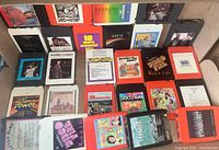 Overview photo showing approximately 25 assorted 8-track tapes laid out flat in multiples rows, highlighting the colorful cases and album covers from the 1970s and 1980s.
