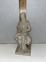 Front view of the porcelain Moses figurine seated, showing detailed beard, robes, and tablet, approximately 7 inches tall seen against a ruler.