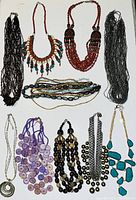 Top-down image showing a variety of colorful beaded necklaces arranged flat, including multiple strands and pendants, in colors black, red, turquoise, purple.