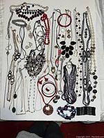 Top-down view of over 55 assorted jewelry pieces including necklaces, bracelets, earrings, and rings laid out on a white surface