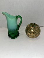 Green and white gradient glass creamer pitcher with spout and handle, and small gold ormolu art glass vase side by side on white background.